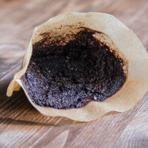 Used coffee filter filled with damp coffee grounds resting on a wooden surface.