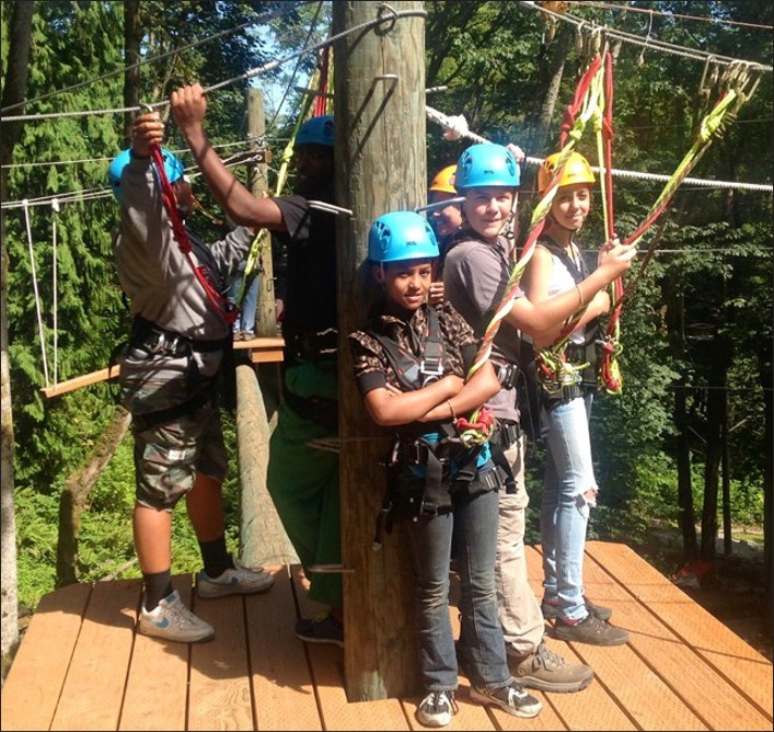 A group of children harnessed to ropes on an elevated platform in the wilderness.