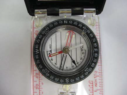 Baseplate compass with a circular bezel and red needle, lid open; rulers in inches/centimeters along the transparent base.
