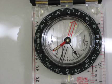 Baseplate compass with bezel marked N-E-S-W, red needle centered, on a clear base with inch/centimeter rulers.