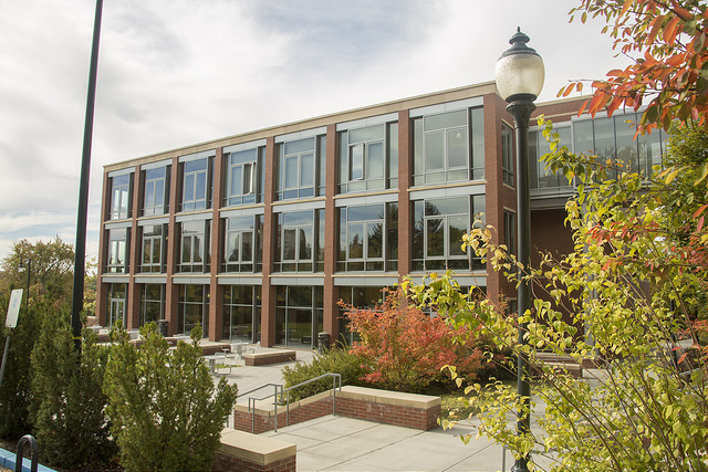 A three story brick building with many windows, surrounded by plants and walkways.