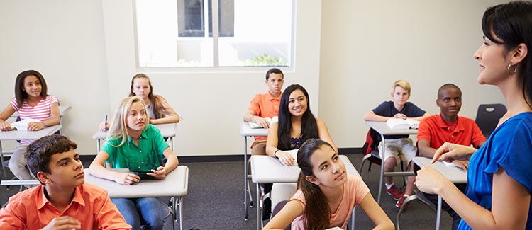 Middle school students sitting at their desks looking at their teacher.