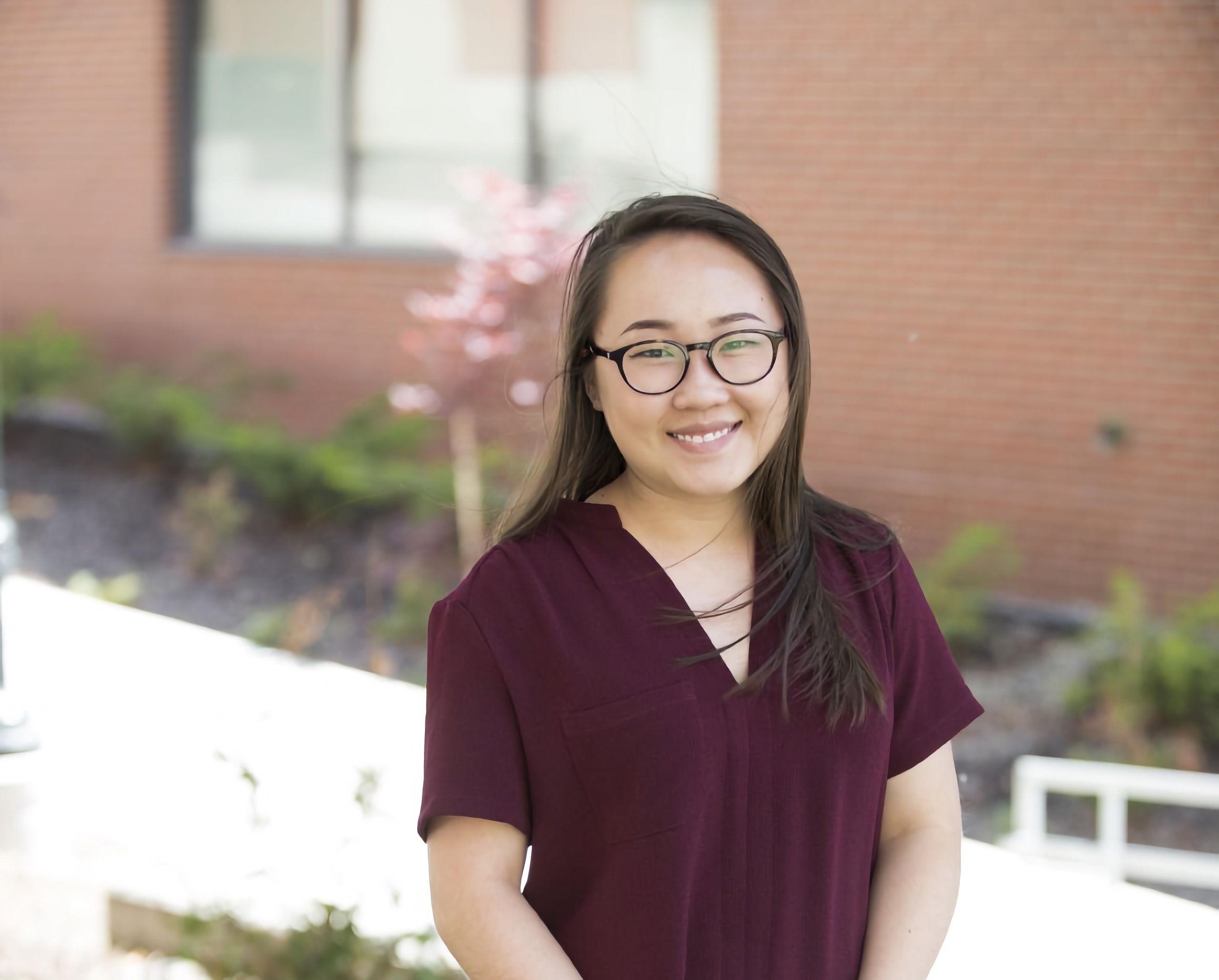 An image of Thao Vo standing outside, smiling and wearing a maroon dress.