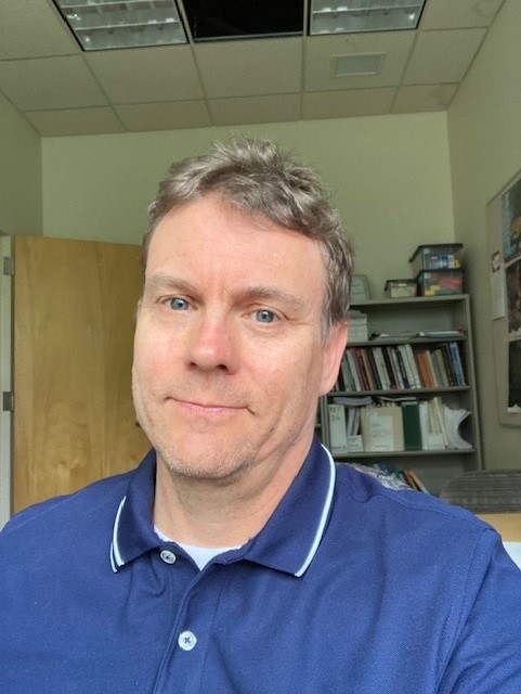 An image of Paul Strand in a blue collared shirt.