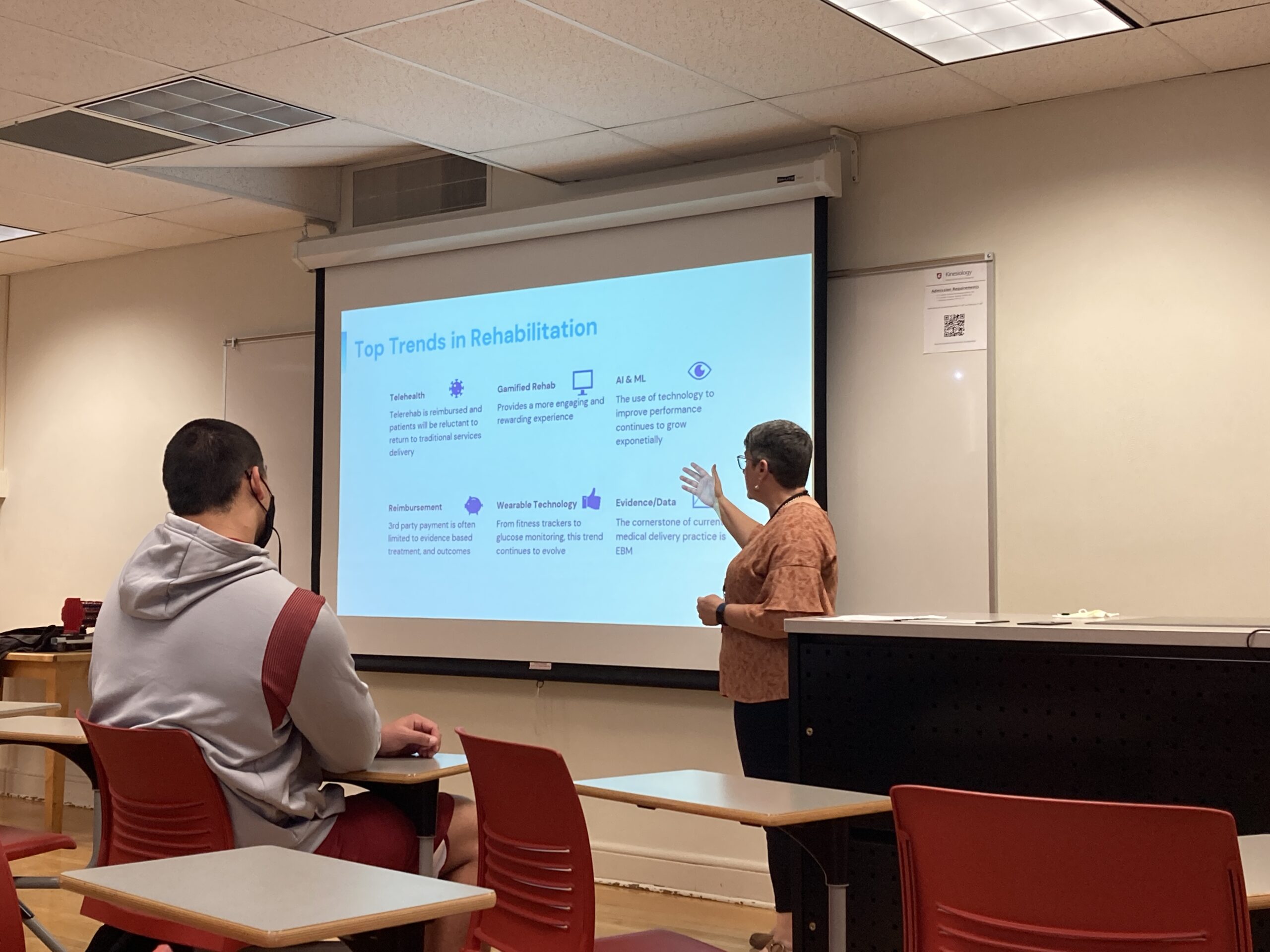 Classroom with one seated person and one at the whiteboard