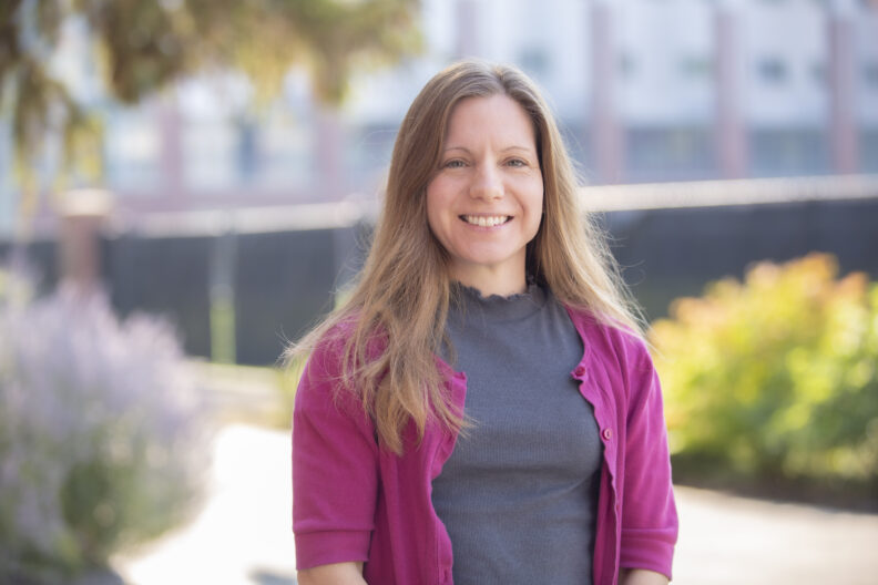 Photo of Amber Brown smiling at camera, the WSU football ops building in the background.