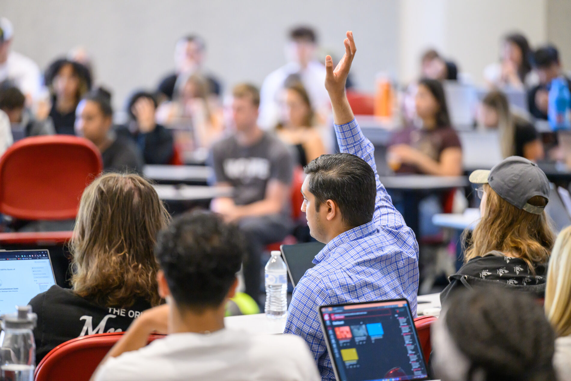 Students in a classroom during a lecture, with one raising a hand.