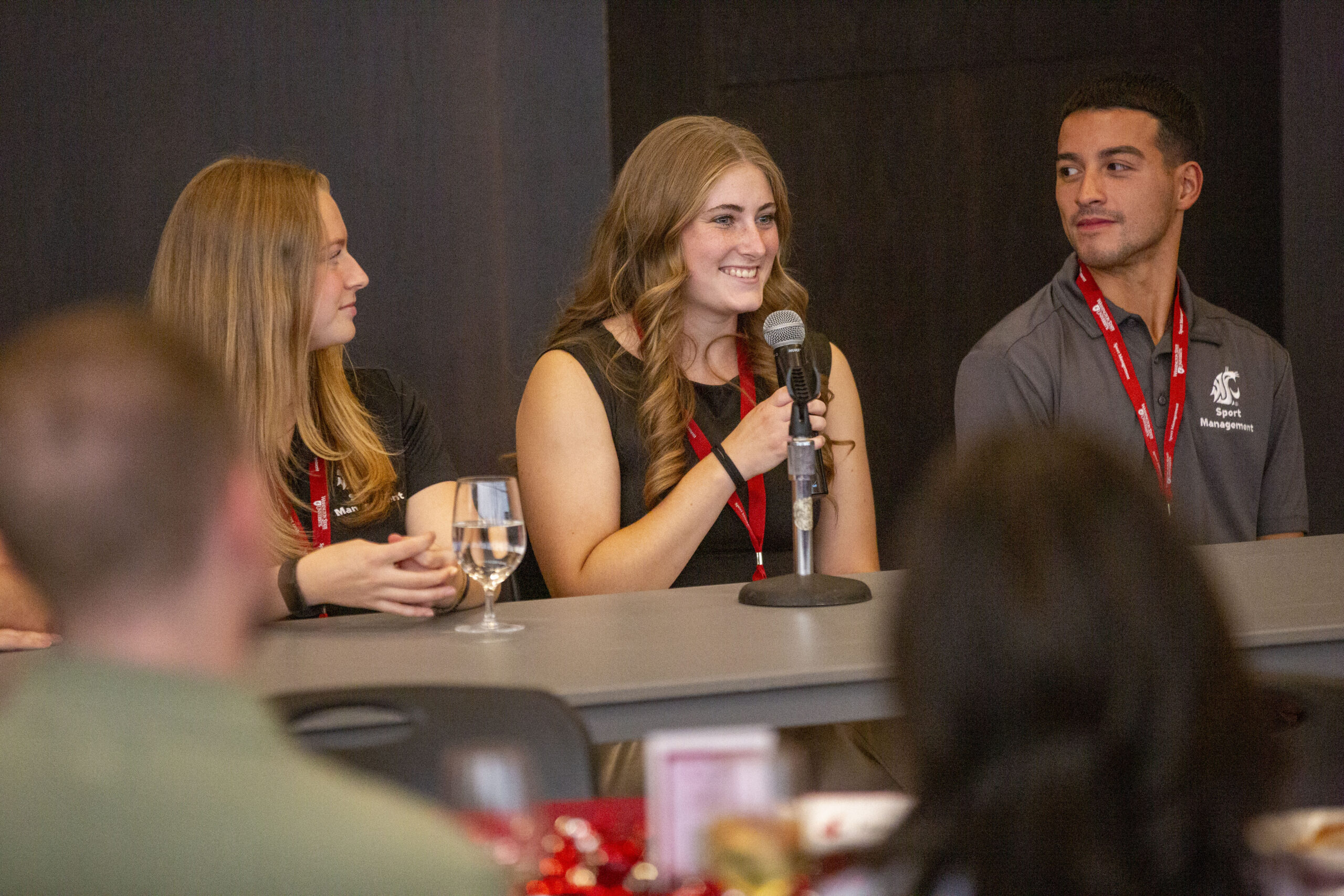 Three student at the desk one holding a mic
