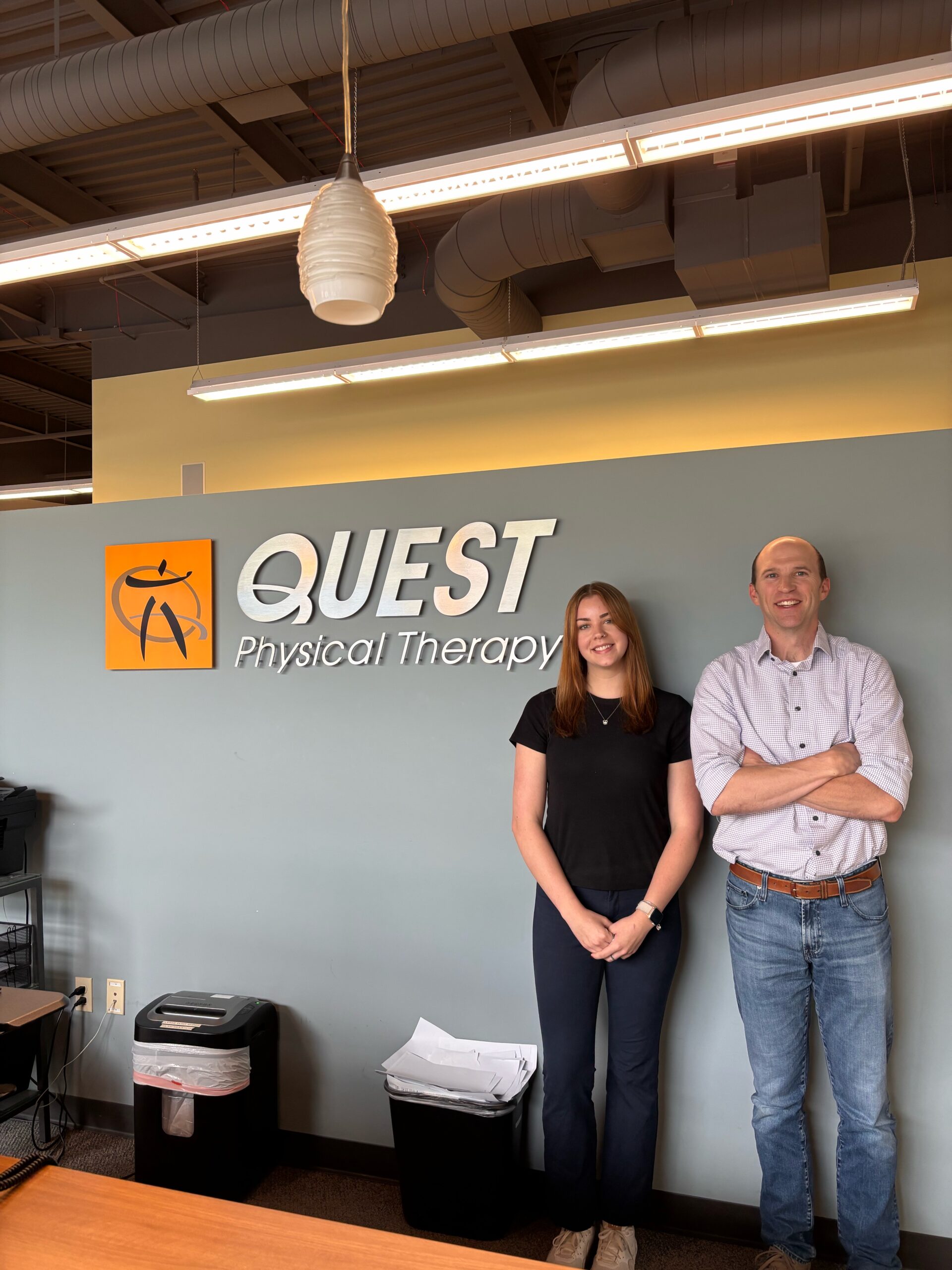 Two people standing next to a QuestPT sign