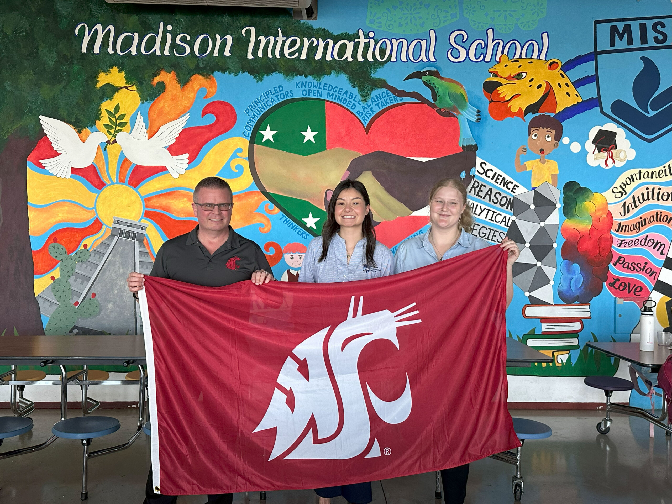 Eric Johnson with two students, standing in Mexico behind a WSU Cougar flag.