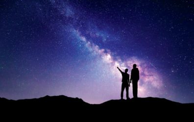 two people in front of a space background with one pointing towards the sky