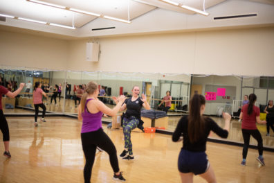 Photo of a Zumba class with six women with their right foot and hands up in the air.