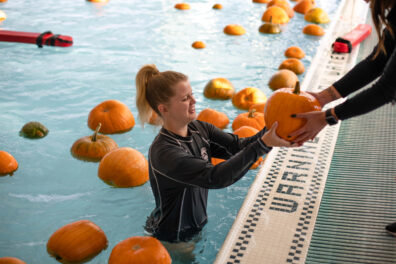 student in pool handing pumpkin