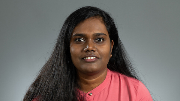 Cynthia in a photo studio with a gray background. She's wearing a coral colored top.