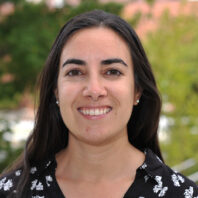 Dr. Fernandez outside with trees and bushes behind her.