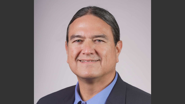 Dr. Warne, wearing a dark suit jacket and light blue button up shirt..