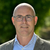 Dr. Arno Werners outside on a sunny day. He's wearing a grey jacket with a light blue button up shirt.