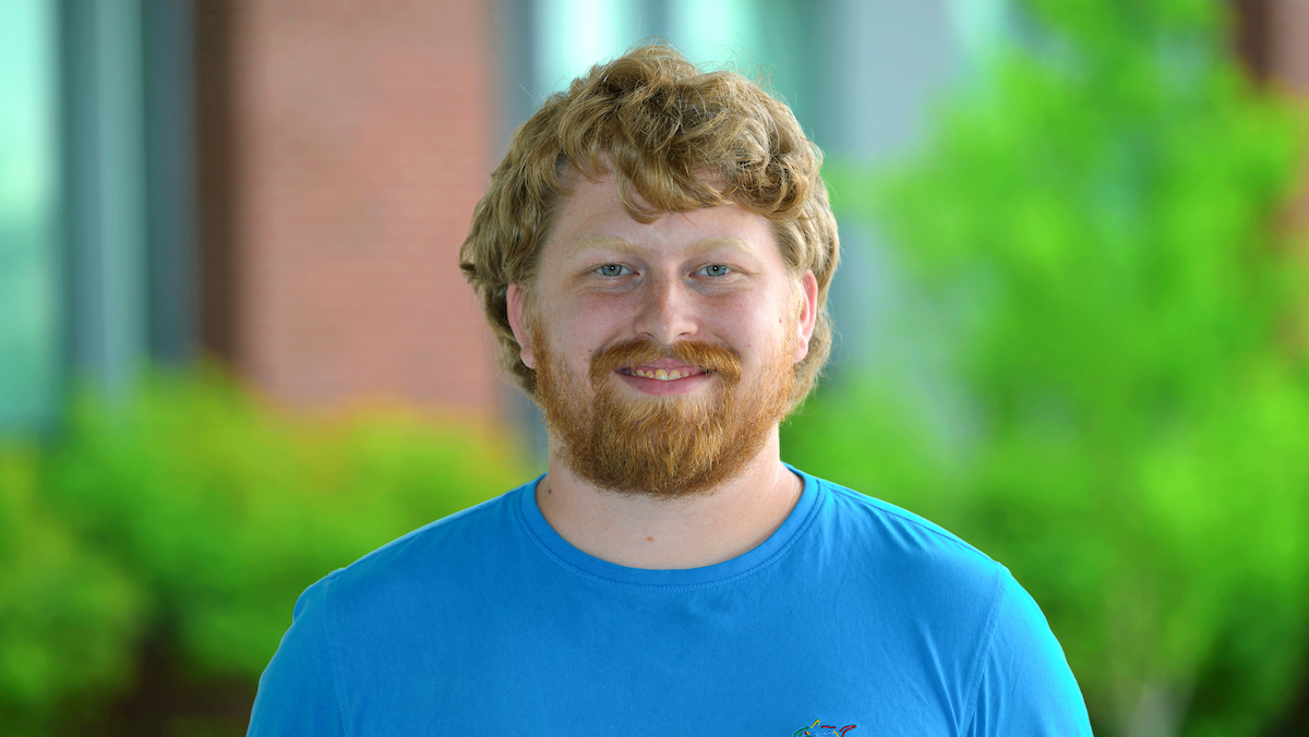 Adam, outside on sunny day. He's wearing a bright blue tshirt.