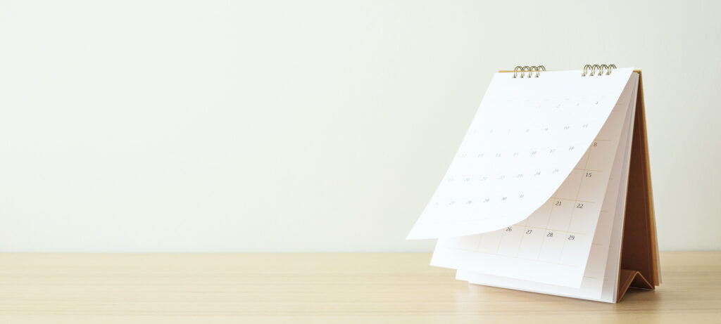 Monthly calendar sitting on wood desk in front of neutral colored background.