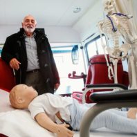 A model child patient lying on a medical bed with a person standing behind it.