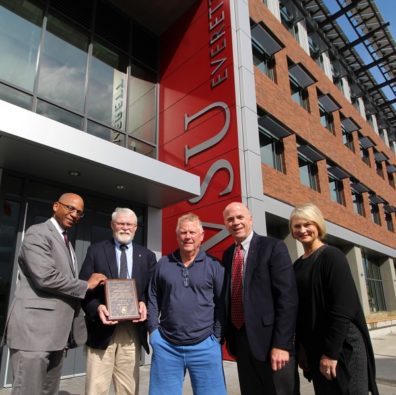 Five people standing in front of a WSU sign and building, one is holding an award.