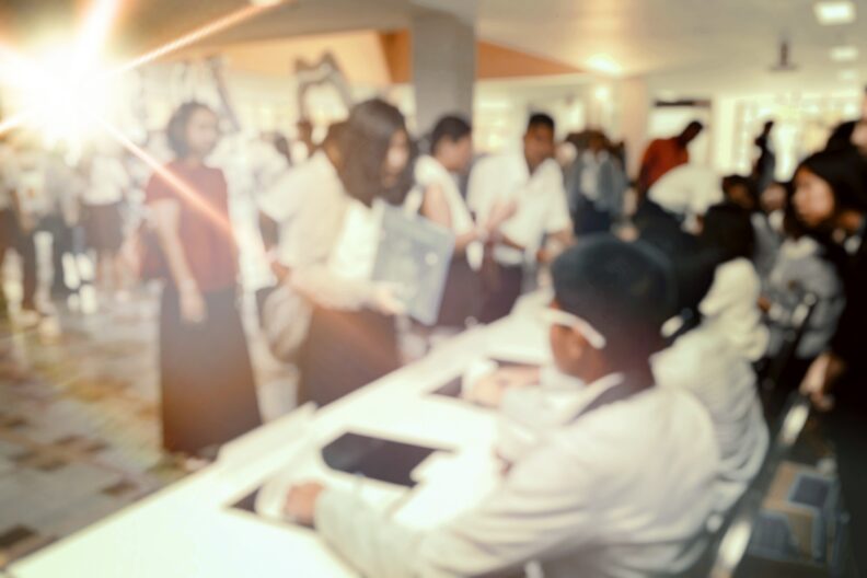 People sitting at a long table while others come up to the table for information.