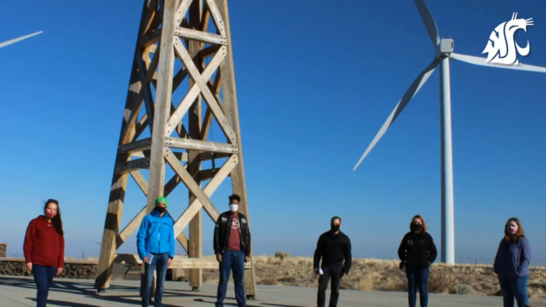 A group of people standing outside in front of a wooden post-and-beam tower.