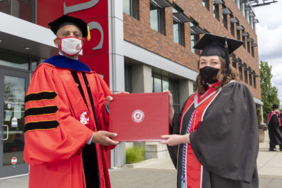 Chancellor Pitre and Claire Jackson wearing graduation robes and posed with a diploma.