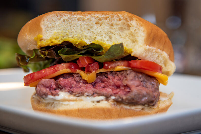 A cross-section of a hamburger with lettuce, cheese, and other toppings showing a raw pink interior.