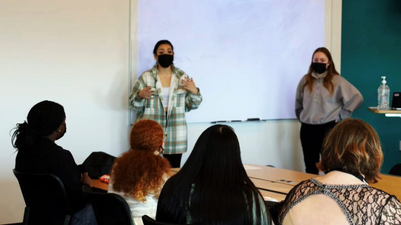 Two people standing in front of a group of other people giving a presentation.