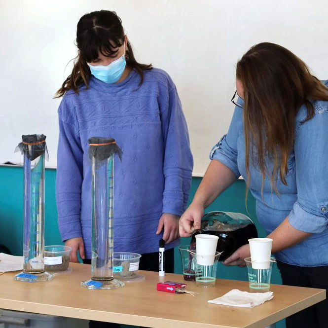 Two  people working at a table with paper cups and measuring beakers.
