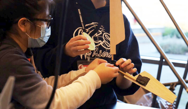 Two people working together to build a wooden fan blade.