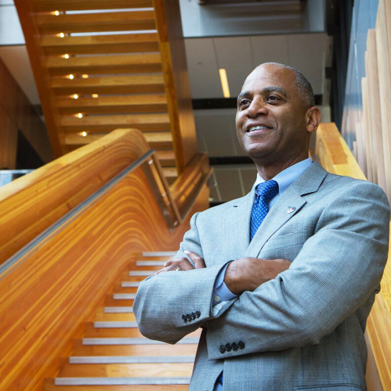 Paul Pitre wearing a gray suit and blue tie, standing with his arms crossed.