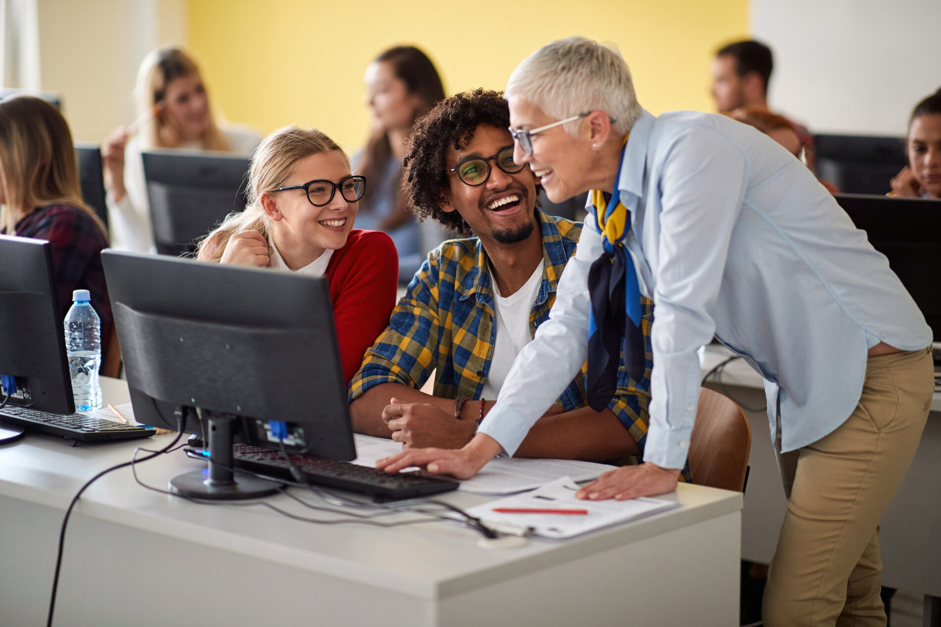 Three people at a computer screen smiling and laughing.
