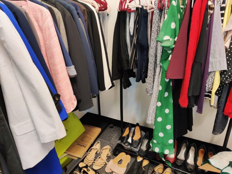 Business clothes hanging on racks over formal shoes.