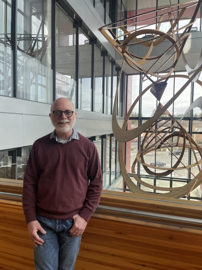 A man in a red sweater standing in front of a large handing sculpture.