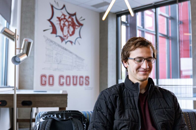 A smiling student sitting on a couch in a room with Go Cougs painted on the wall.