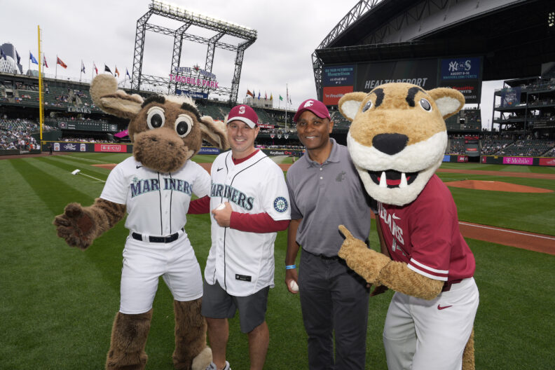 Chancellor Paul Pitre and Coach Dickert (wearing a Mariners jersey shirt) posing with the Mariners moose mascot and the WSU cougar mascot on a baseball field.