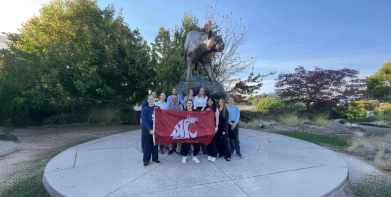 Camille Orego (center) holds the WSU flag with members of the Society of Women Engineers (SWE) in front of the Cougar Pride statue.
