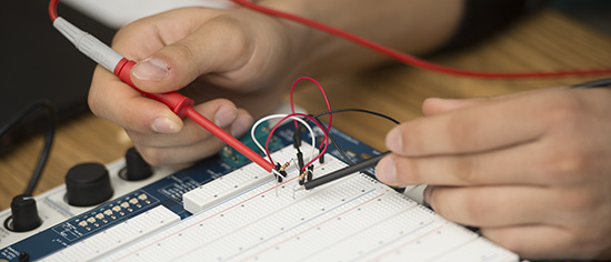 Close-up of hands testing circuits on a breadboard.
