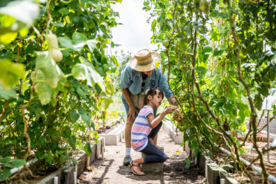 Older person mentoring young girl in a garden.