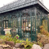 Green metal greenhouse w/urns outside at 2025 Annual Garden Tour