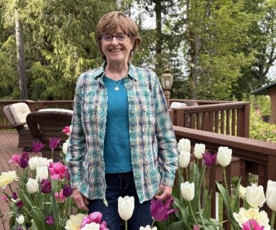 Master Gardener Margery Whites stands on a wooden deck surrounded by potted tulip plants.