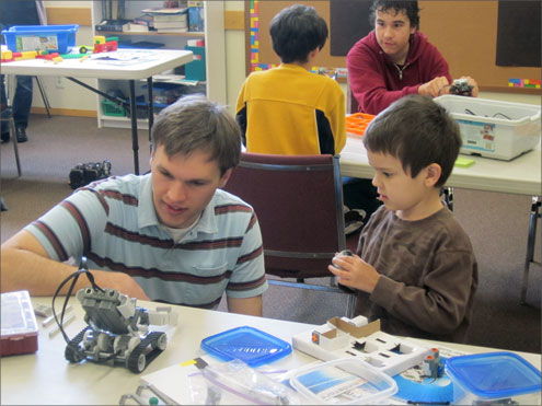 child and adult working on a robot in a classroon