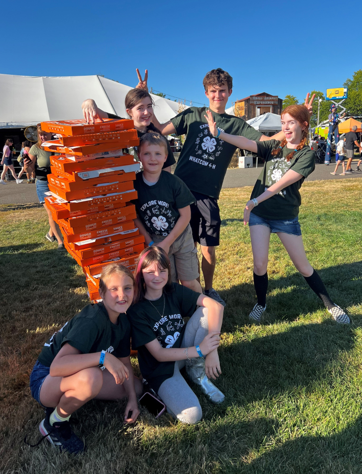 4-H members posing for the camera with a large stack of pizzas.