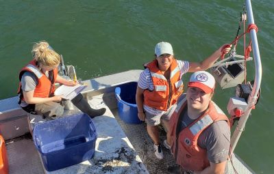 Three people in a boat using bottom sampling equipment.