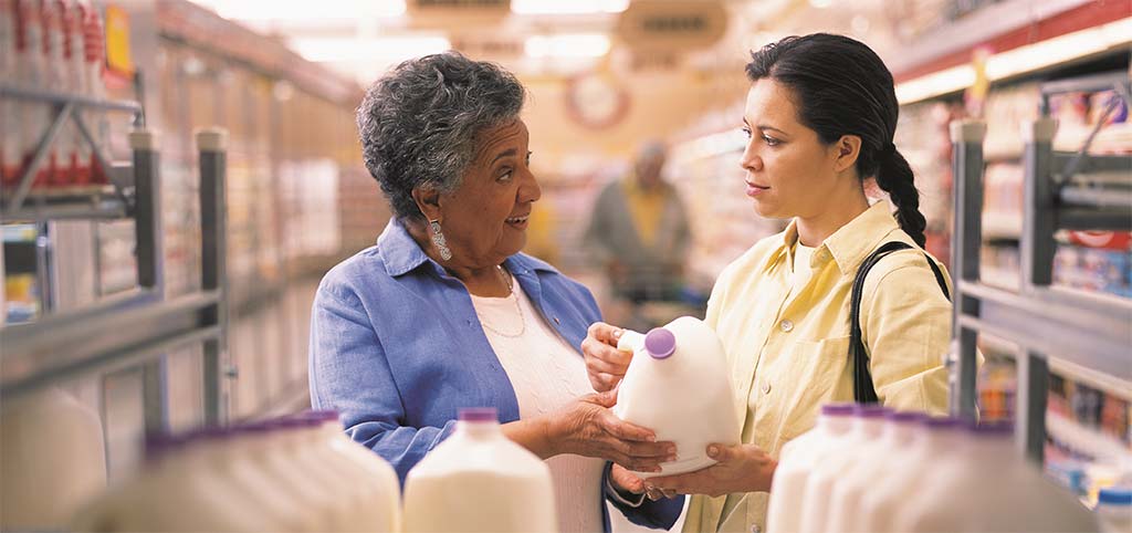 Two women at store look at nutrition on milk