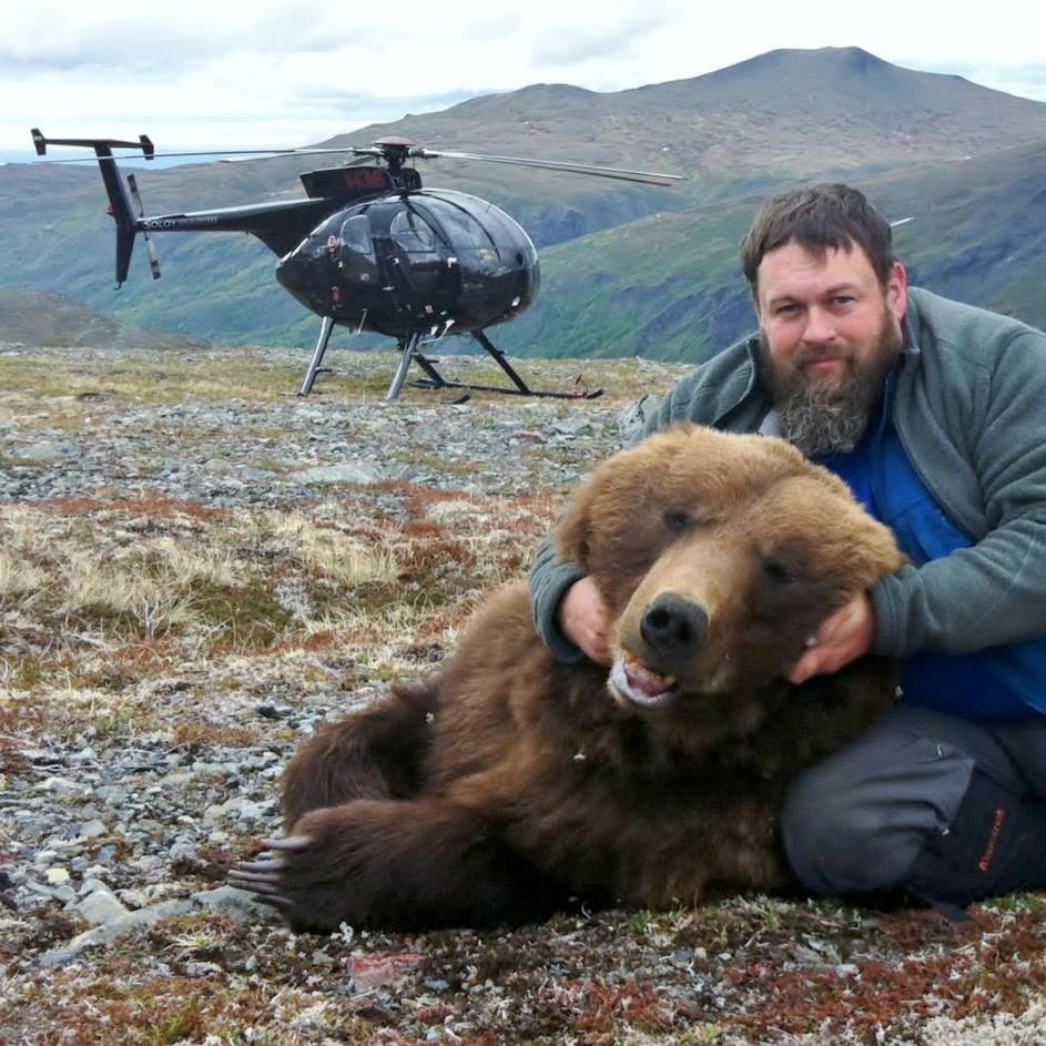 Tony Carnahan holding the head of a drugged bear with a helicopter in the background.