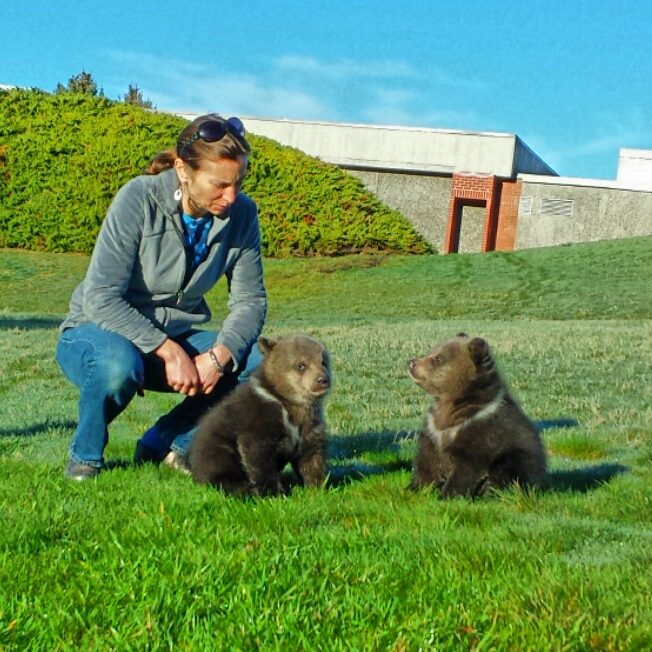 Nina Woodford in a grassy field with two bear cubs.