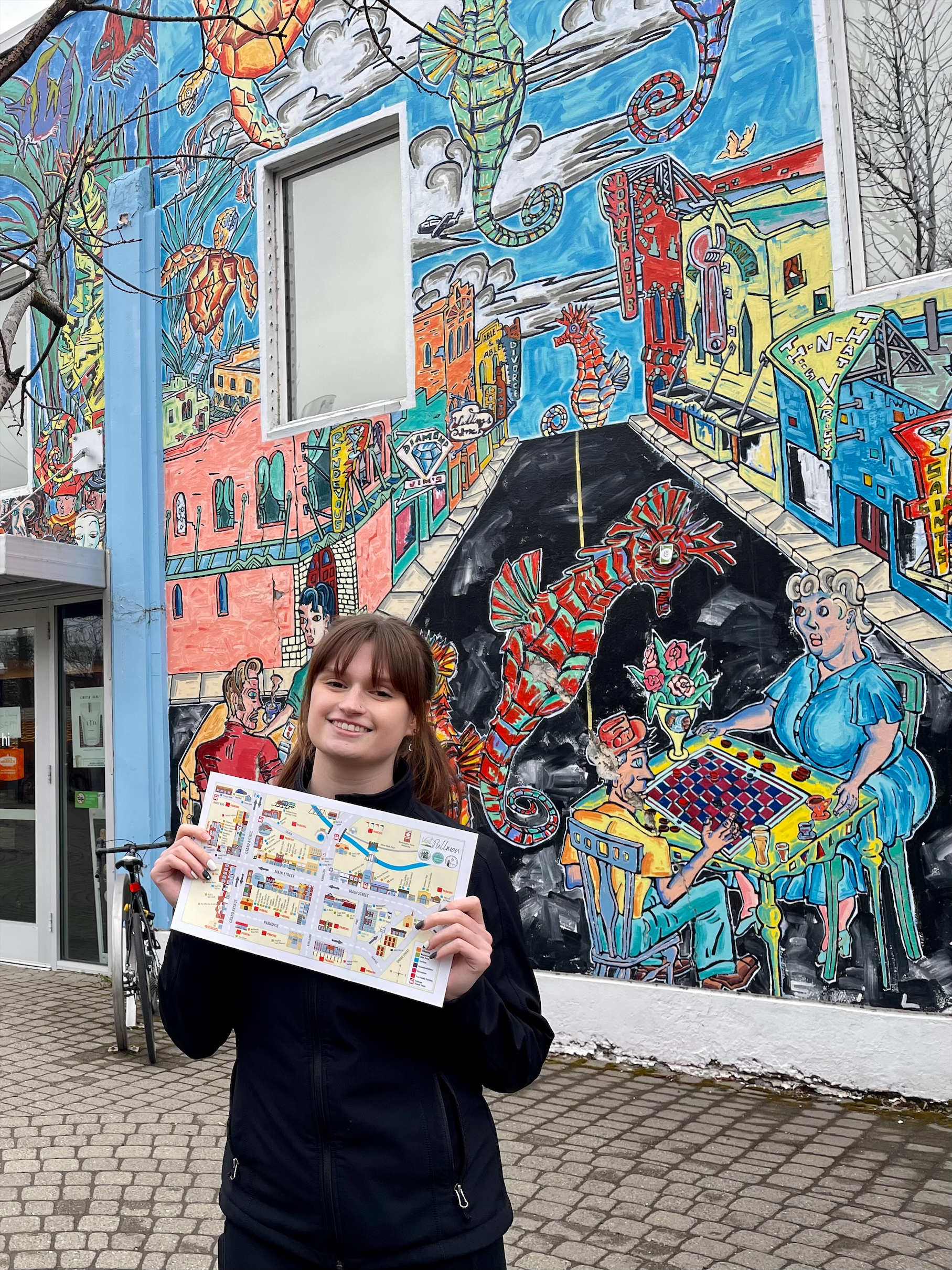 A Brelsford Washington State University Visitor Center employee holding a Downtown Pullman map in Downtown Pullman public plaza.